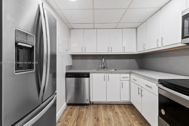 kitchen featuring appliances with stainless steel finishes, white cabinetry, sink, a drop ceiling, and light hardwood / wood-style flooring