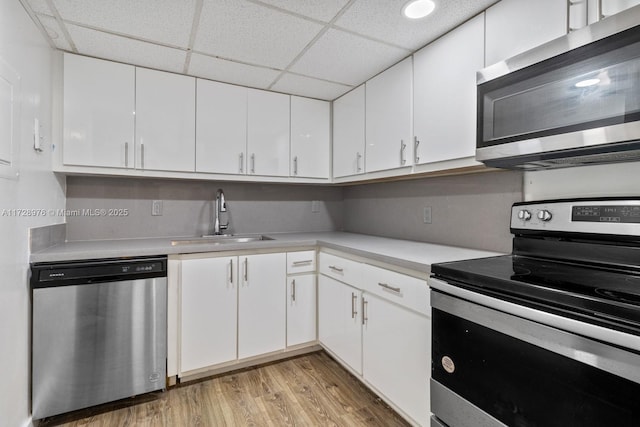 kitchen with white cabinets, a paneled ceiling, stainless steel appliances, light hardwood / wood-style floors, and sink