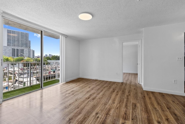 empty room with a textured ceiling, floor to ceiling windows, and hardwood / wood-style floors