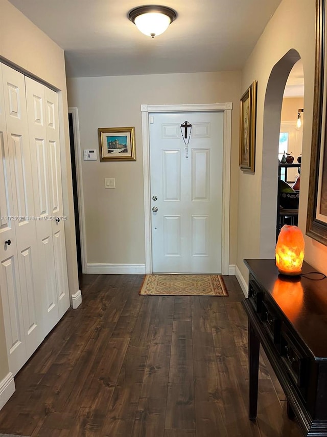 interior space with arched walkways, dark wood-style flooring, and baseboards