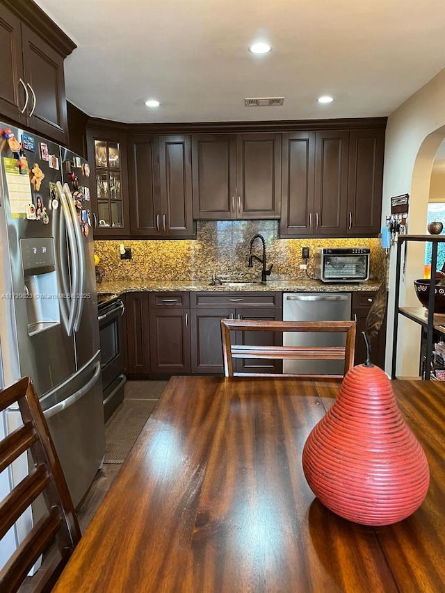 kitchen featuring appliances with stainless steel finishes, dark hardwood / wood-style floors, dark brown cabinets, light stone counters, and sink