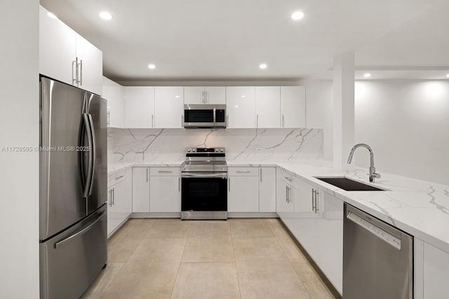 kitchen featuring white cabinetry, kitchen peninsula, stainless steel appliances, light stone countertops, and sink