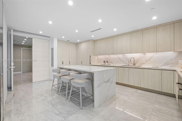 kitchen featuring light stone counters, sink, light brown cabinetry, and a center island