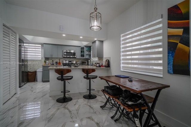 kitchen featuring gray cabinets, appliances with stainless steel finishes, hanging light fixtures, stone countertops, and kitchen peninsula