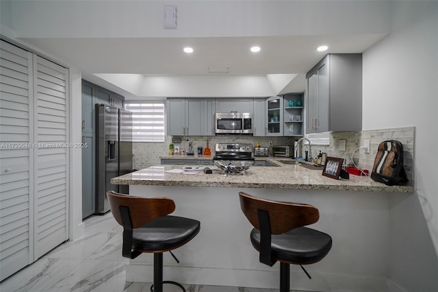 kitchen with appliances with stainless steel finishes, gray cabinetry, light stone counters, and kitchen peninsula