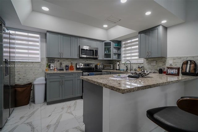 kitchen with stainless steel appliances, gray cabinets, kitchen peninsula, and light stone countertops