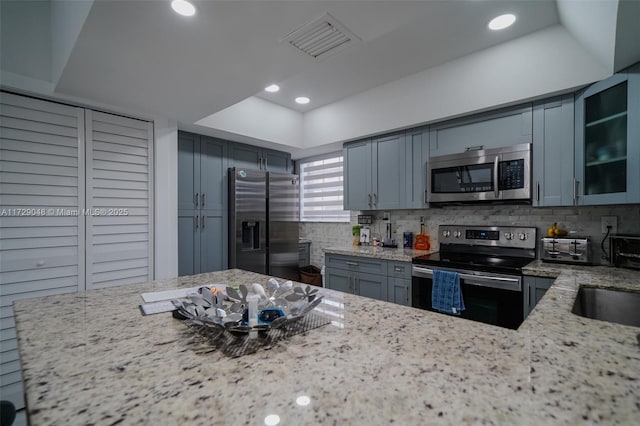 kitchen featuring sink, appliances with stainless steel finishes, a tray ceiling, light stone countertops, and decorative backsplash