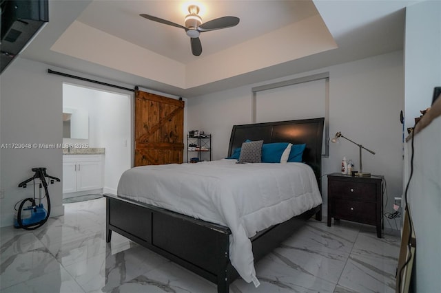 bedroom featuring connected bathroom, a tray ceiling, a barn door, and ceiling fan