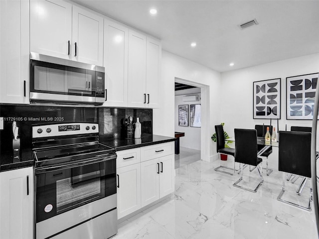 kitchen with appliances with stainless steel finishes, dark stone counters, decorative backsplash, and white cabinets