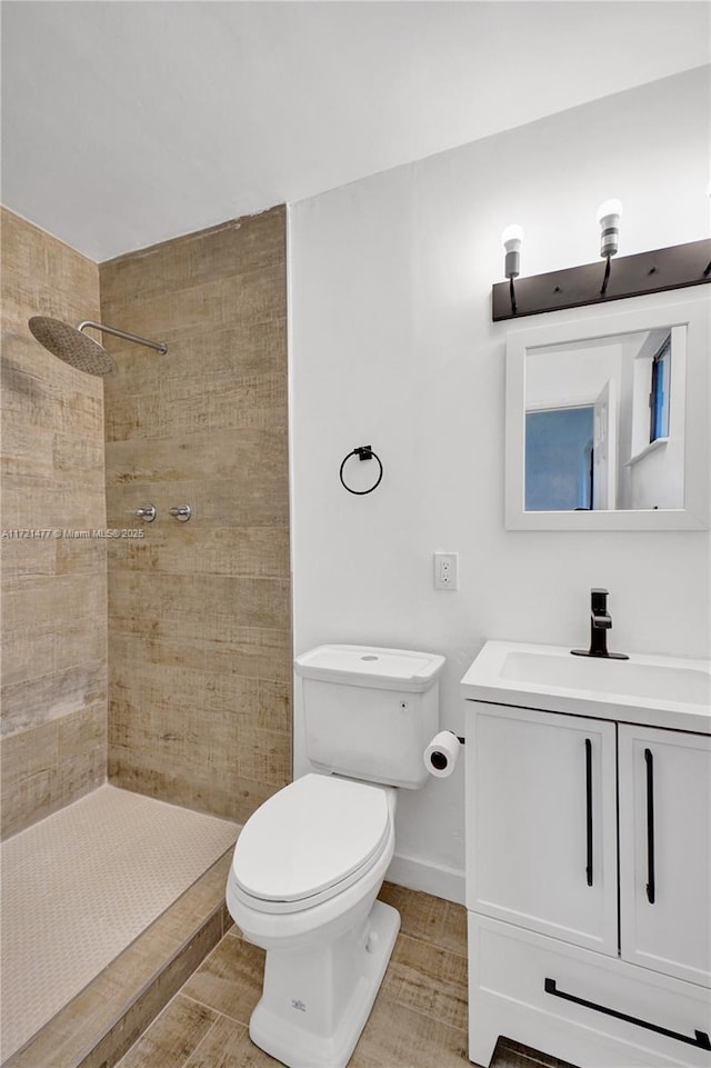 bathroom with toilet, a tile shower, hardwood / wood-style floors, and vanity