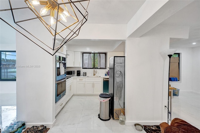 kitchen featuring double oven, sink, a chandelier, and white cabinetry