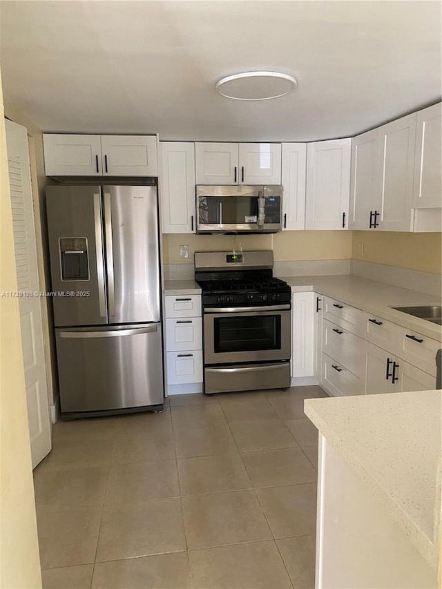 kitchen with tile patterned floors, stainless steel appliances, sink, and white cabinets