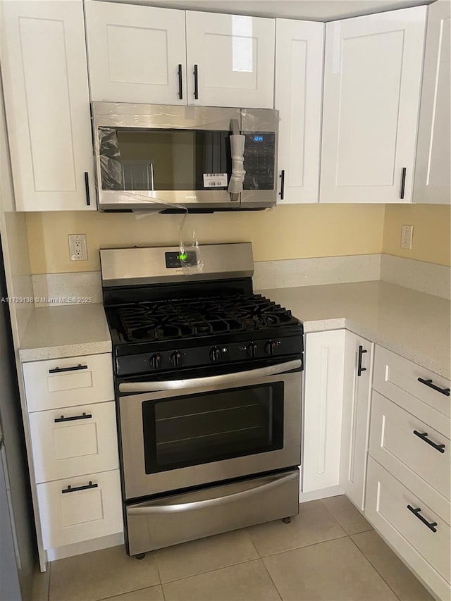 kitchen featuring stainless steel appliances, light tile patterned floors, and white cabinets