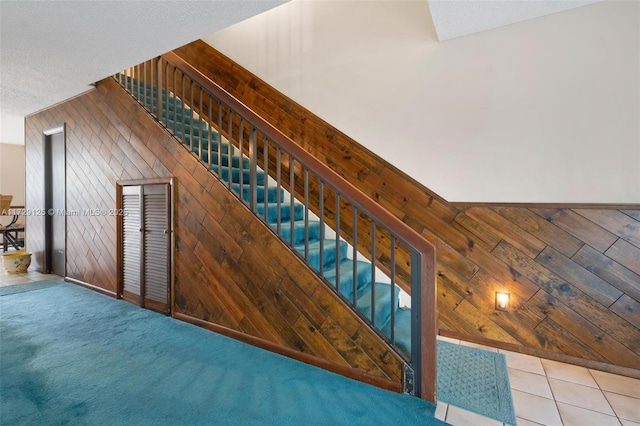 stairs featuring a textured ceiling, tile patterned floors, and wooden walls