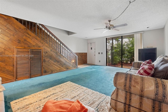 living room featuring a textured ceiling, ceiling fan, carpet flooring, and wooden walls