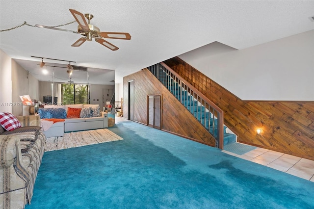 living room with a textured ceiling, ceiling fan, carpet flooring, and wooden walls