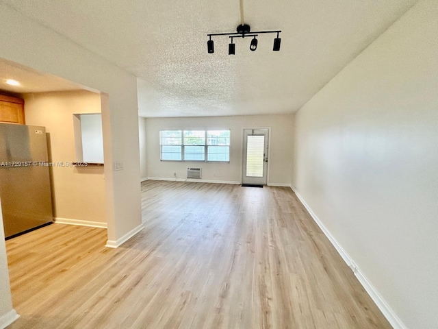 interior space with a textured ceiling, light hardwood / wood-style floors, and a wall unit AC