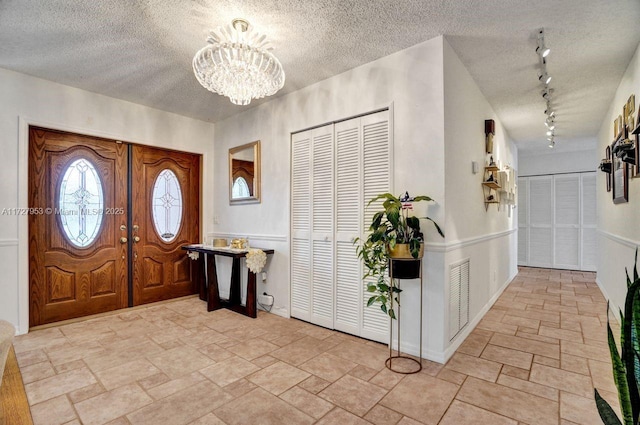 foyer entrance featuring rail lighting, a textured ceiling, and a notable chandelier