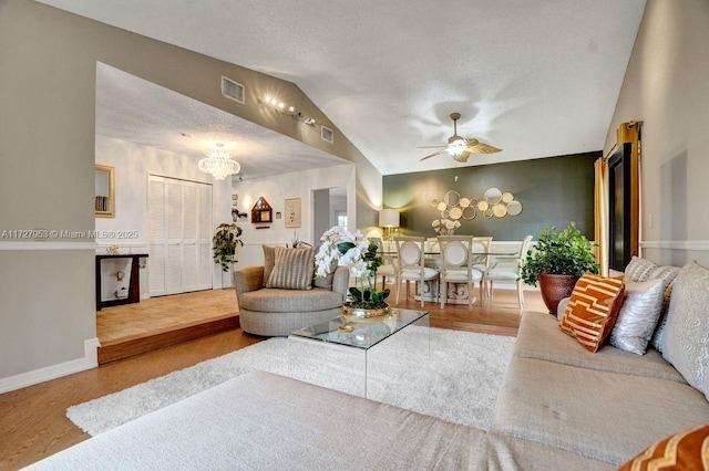 living room featuring a textured ceiling, hardwood / wood-style floors, ceiling fan with notable chandelier, and vaulted ceiling