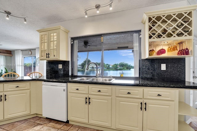 kitchen with a textured ceiling, dishwasher, sink, backsplash, and a water view