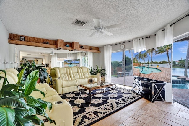 living room featuring ceiling fan, a water view, and a textured ceiling