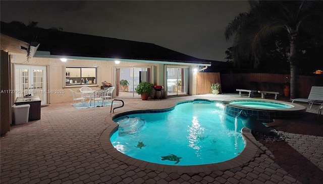 pool at night with pool water feature, an in ground hot tub, a patio, and french doors