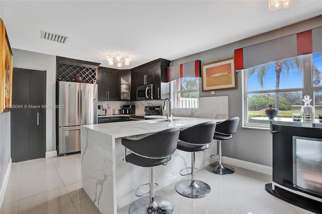 kitchen with a breakfast bar, sink, dark brown cabinetry, light stone countertops, and appliances with stainless steel finishes