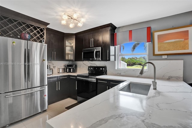 kitchen featuring appliances with stainless steel finishes, backsplash, dark brown cabinets, light stone counters, and sink