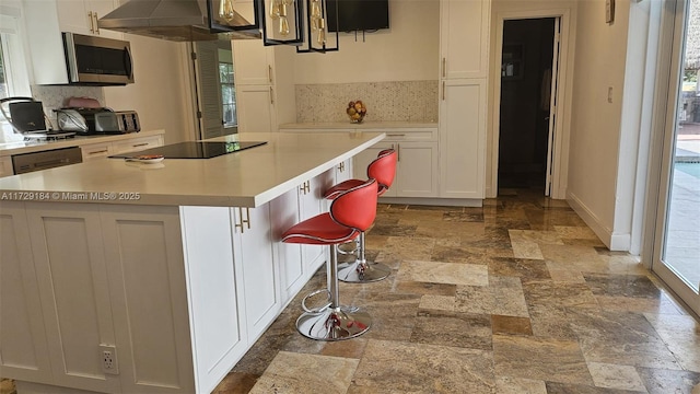 kitchen featuring a breakfast bar, white cabinetry, a center island, black electric stovetop, and backsplash