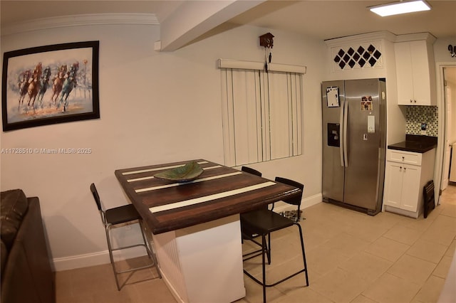 kitchen featuring white cabinetry, tasteful backsplash, stainless steel fridge with ice dispenser, crown molding, and a breakfast bar area