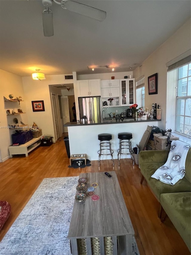 kitchen with white cabinetry, a kitchen bar, kitchen peninsula, hardwood / wood-style flooring, and stainless steel refrigerator