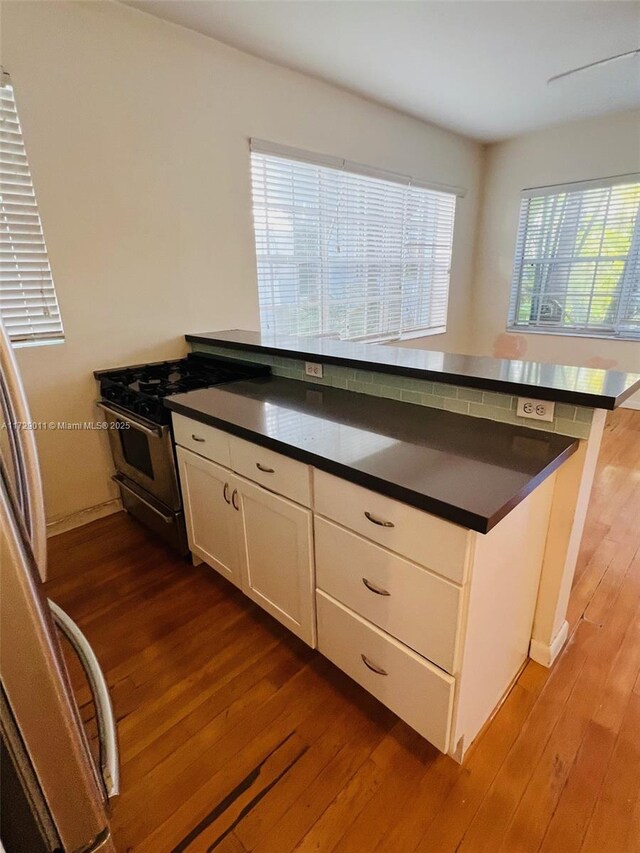 kitchen with white cabinets, stainless steel refrigerator, kitchen peninsula, light wood-type flooring, and a breakfast bar