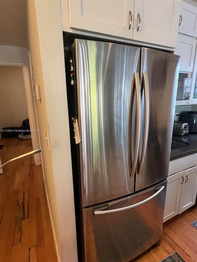 kitchen with light wood-type flooring, stainless steel fridge, and white cabinetry