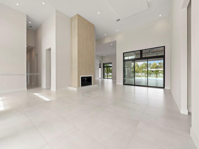 unfurnished living room with a fireplace, light tile patterned floors, and a towering ceiling