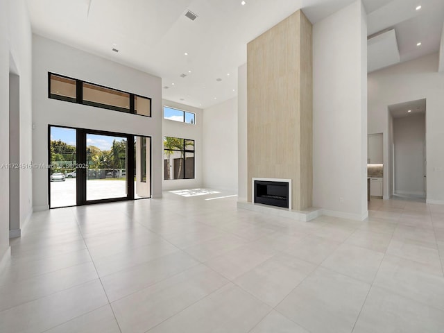 unfurnished living room with light tile patterned flooring, a large fireplace, a towering ceiling, and french doors