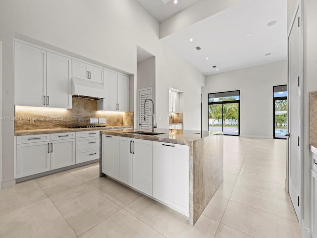 kitchen with white cabinets, an island with sink, decorative backsplash, sink, and stone countertops