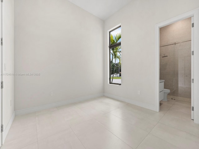 unfurnished bedroom featuring ensuite bathroom, a walk in closet, and light tile patterned flooring