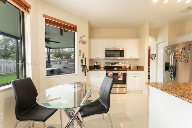 kitchen with light tile patterned floors, ceiling fan, appliances with stainless steel finishes, dark stone counters, and white cabinets