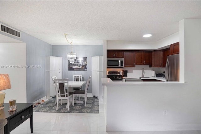 kitchen with a textured ceiling, appliances with stainless steel finishes, sink, hanging light fixtures, and kitchen peninsula