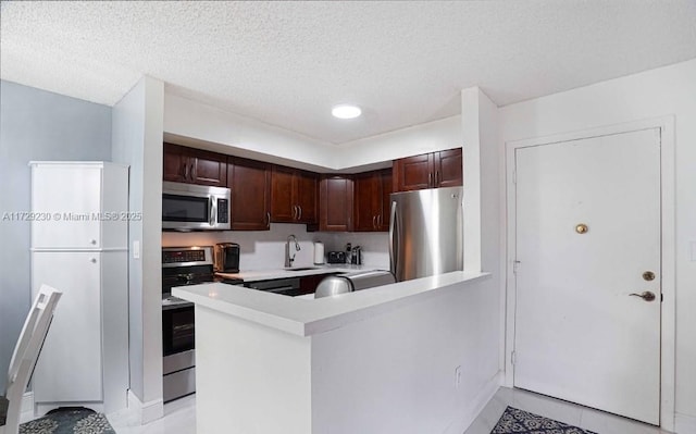 kitchen with a textured ceiling, light tile patterned floors, appliances with stainless steel finishes, and kitchen peninsula