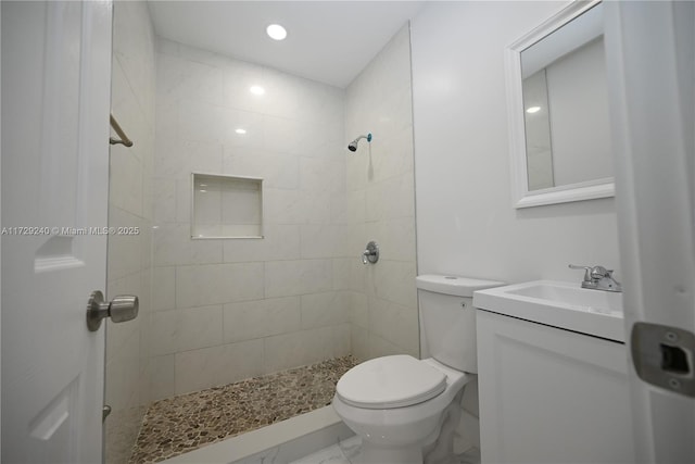 bathroom featuring toilet, a tile shower, and vanity