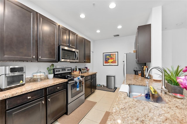 kitchen with sink, light stone countertops, appliances with stainless steel finishes, light tile patterned floors, and dark brown cabinets