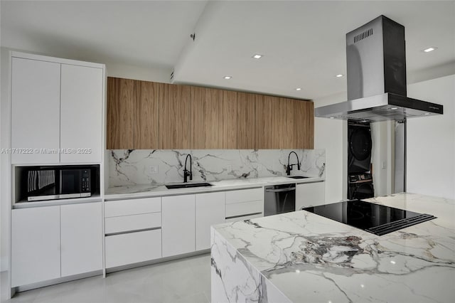 kitchen featuring sink, white cabinets, island exhaust hood, stacked washer / dryer, and black appliances