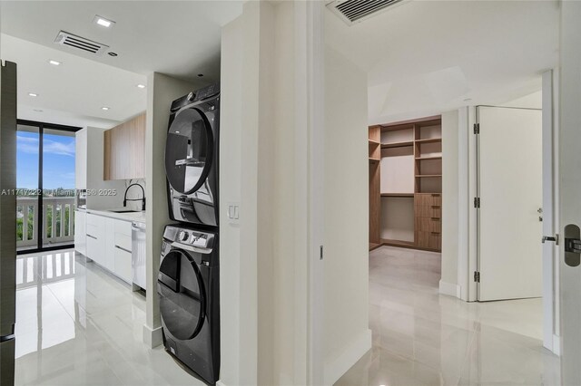 laundry area featuring stacked washing maching and dryer, sink, and light tile patterned floors