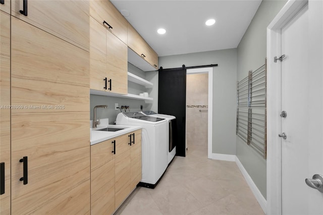 clothes washing area featuring washer and clothes dryer, cabinets, sink, light tile patterned floors, and a barn door