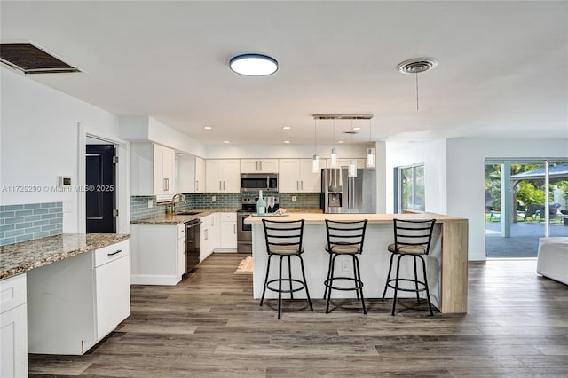 kitchen featuring a center island, sink, stainless steel appliances, white cabinets, and light stone counters