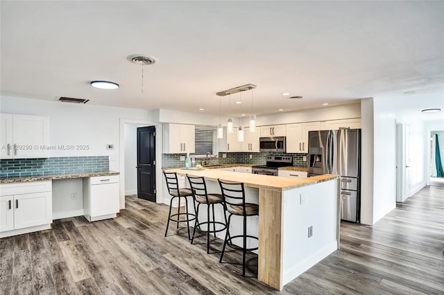 kitchen with hanging light fixtures, appliances with stainless steel finishes, white cabinetry, and a kitchen island