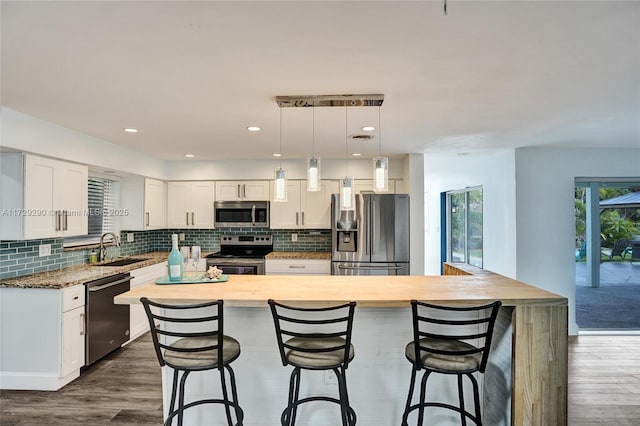 kitchen with appliances with stainless steel finishes, a kitchen island, decorative light fixtures, white cabinetry, and sink