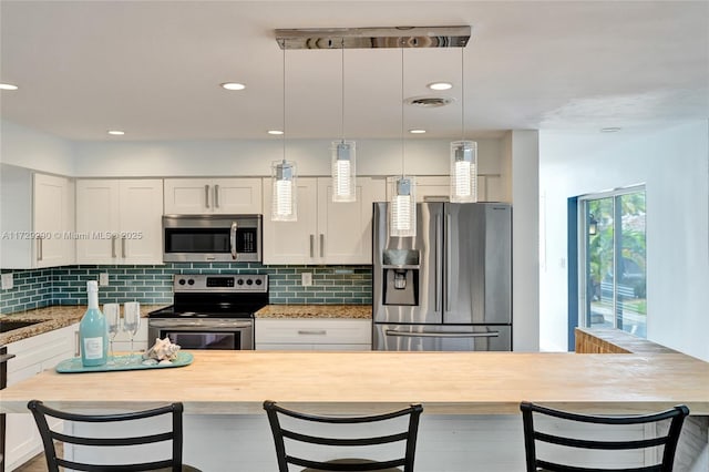 kitchen featuring backsplash, hanging light fixtures, light stone countertops, stainless steel appliances, and white cabinets