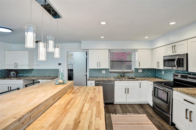 kitchen featuring decorative light fixtures, butcher block countertops, white cabinets, and stainless steel appliances